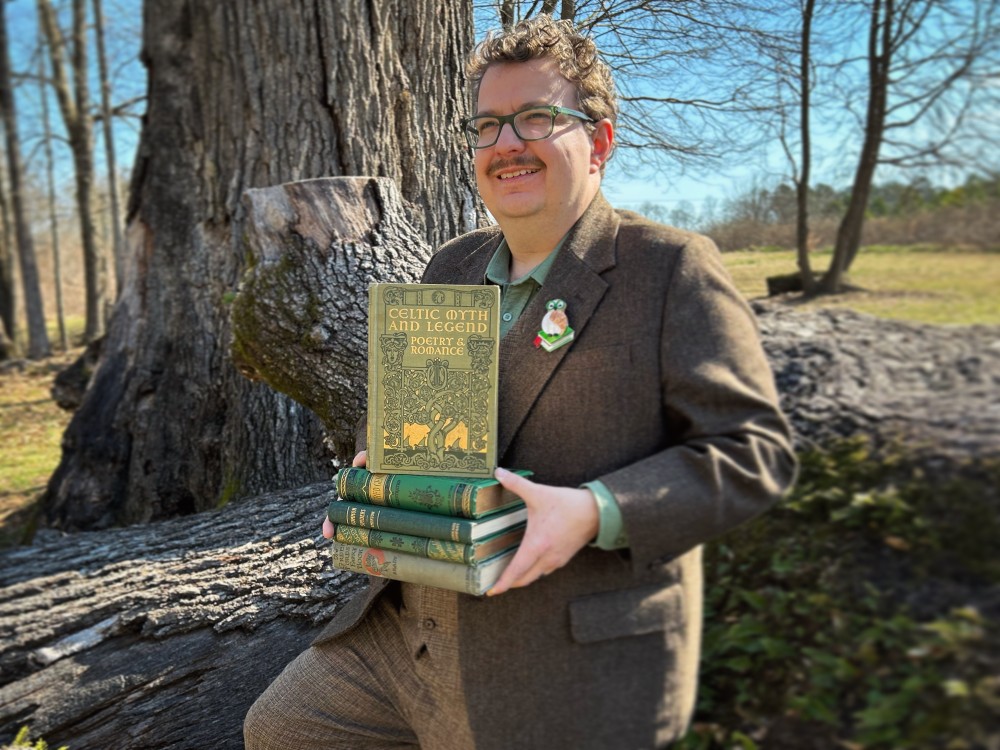 Josh holding a stack of rare books with a tree in the background